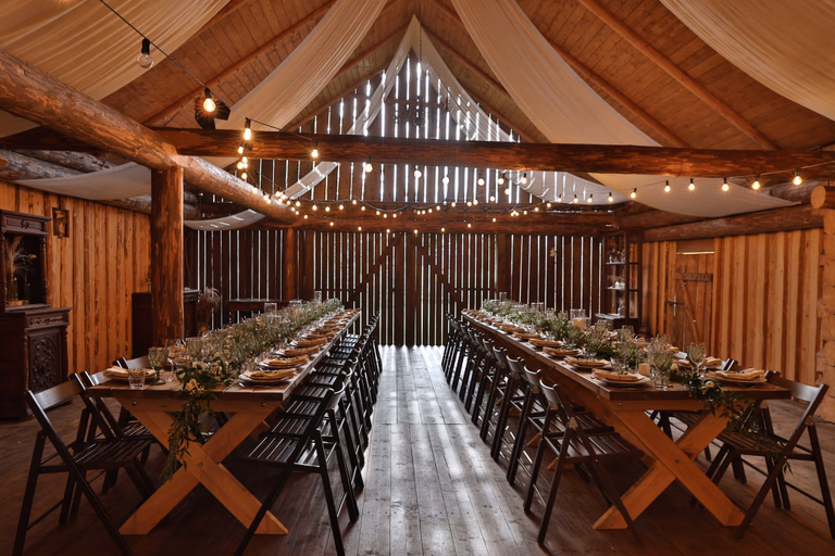 Barn reception hall with long farm tables, greenery runners, and ceiling drapery