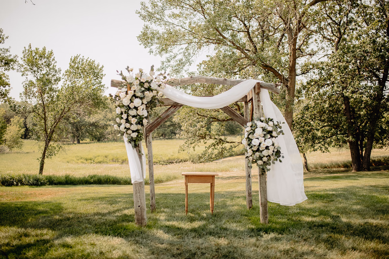 Wooden wedding arch with white drapery and flowers standing in an open meadow