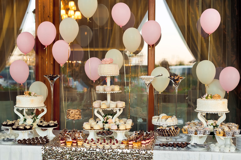 Dessert table decorated with pastel balloons and tiered stands of sweets