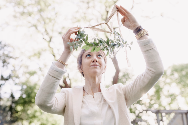 An event planner lifting a handmade greenery wreath while styling an outdoor celebration